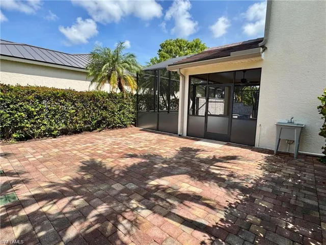 Expansive paver patio featuring a screened enclosure, stucco exterior, and mature hedge landscaping