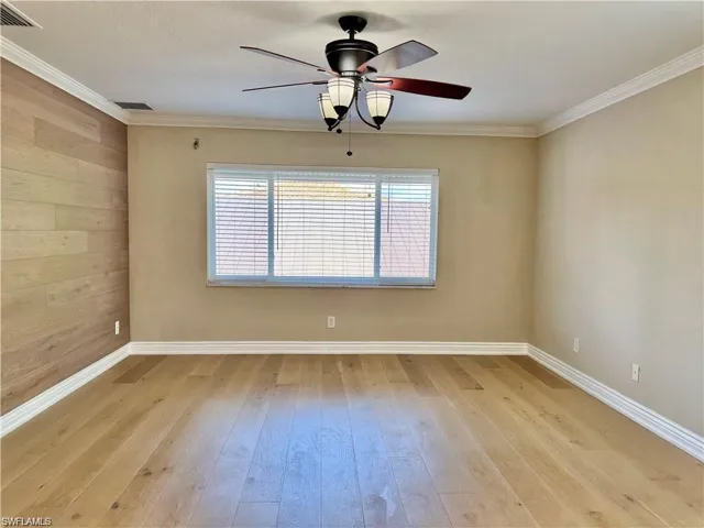 Room featuring wood-finish flooring, a decorative accent wall, crown molding, and an overhead ceiling fan with integrated lighting