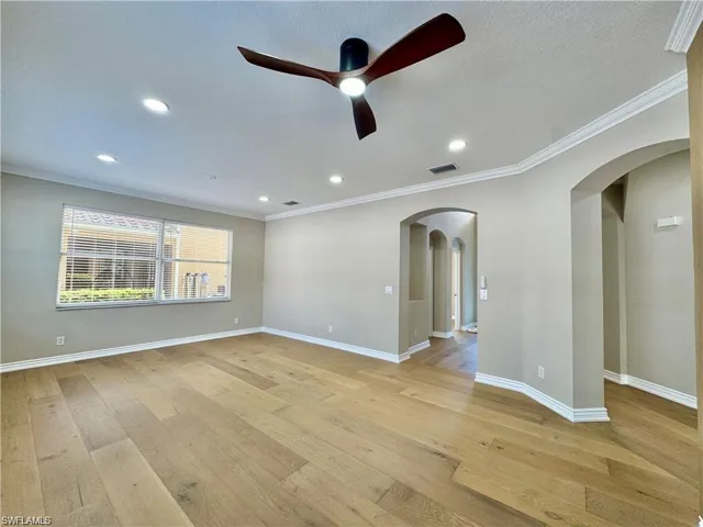 Spacious room featuring wood-finish flooring, recessed lighting, a modern ceiling fan, and arched doorways