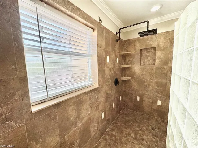 Tiled shower enclosure featuring a dark-finish rainfall showerhead, built-in shelving, and a recessed niche
