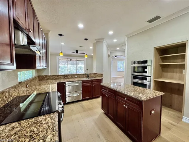 Gourmet kitchen featuring granite countertops, rich wood cabinetry, stainless steel appliances, a built-in oven and microwave, and light wood-finish flooring