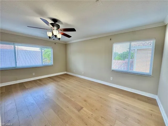 Spacious room featuring wide plank wood-finish flooring, two large windows with blinds, a ceiling fan with integrated lighting, and crown molding