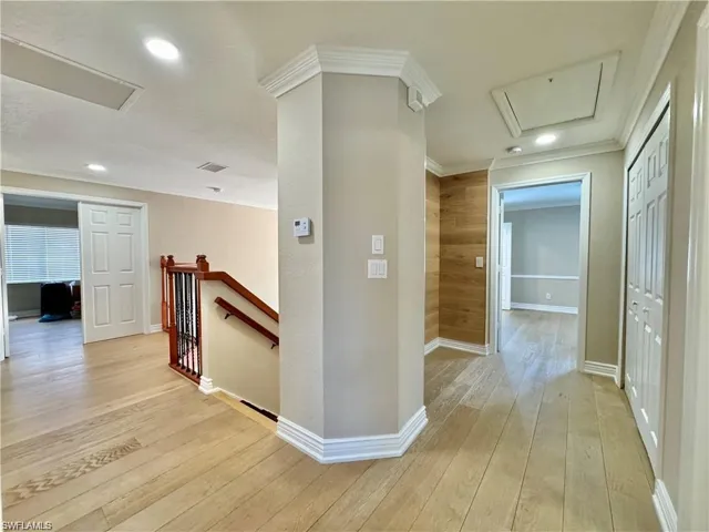 Hardwood flooring throughout the upper hallway, featuring recessed lighting, crown molding, and a wood-paneled accent wall
