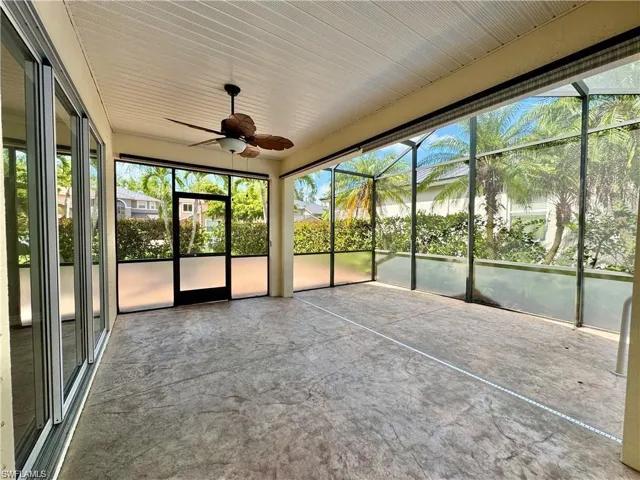 Expansive screened outdoor living area featuring a ceiling fan with light, textured concrete flooring, and surrounding tropical foliage