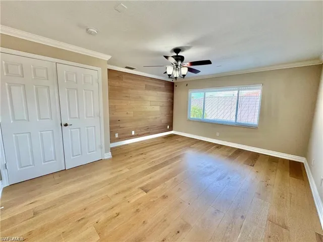 Open room featuring wood-finish flooring, a decorative accent wall, and a ceiling fan with integrated lighting