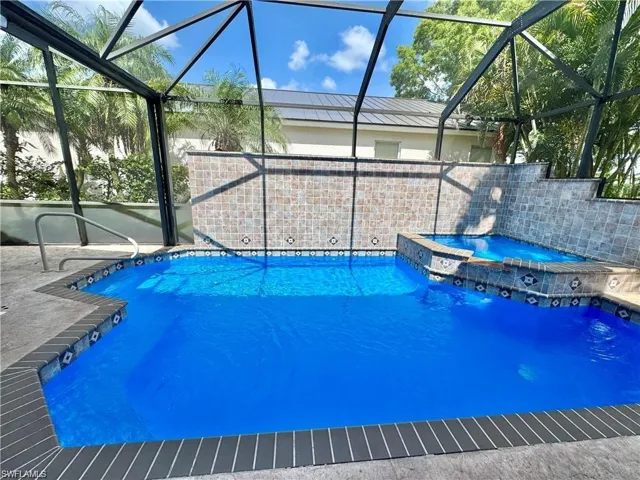 Screened pool area featuring a blue-tiled pool, an integrated spa, and a tiled water feature wall