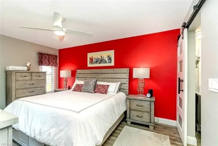 Bedroom featuring dark wood-type flooring, a barn door, and a ceiling fan