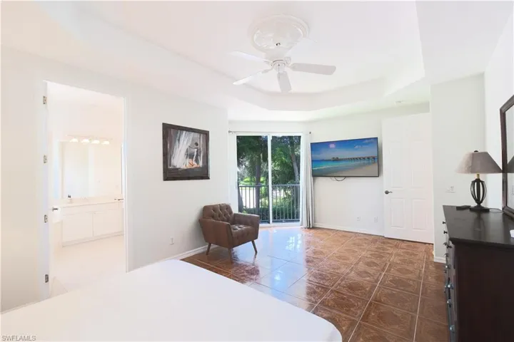 Bedroom featuring a raised ceiling, connected bathroom, tile floors, and access to outside