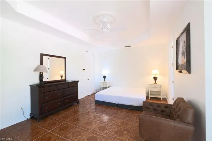 Tiled bedroom featuring ceiling fan and a tray ceiling