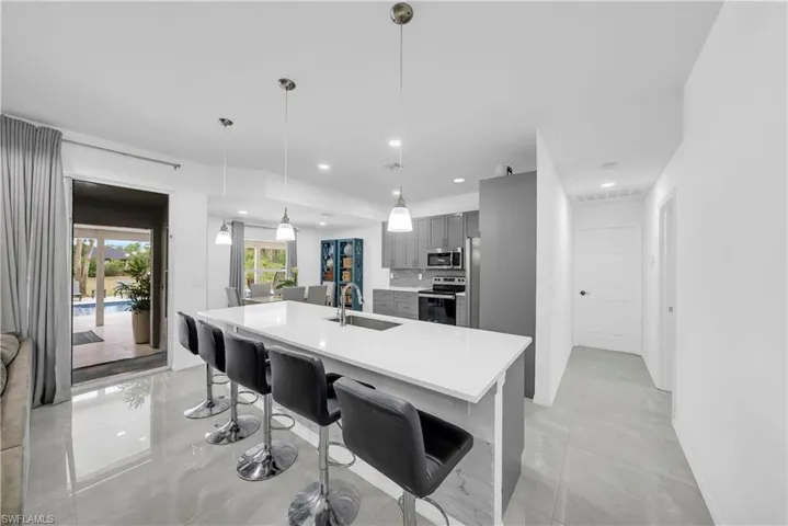 Kitchen featuring gray cabinetry, stainless steel appliances, a kitchen breakfast bar, hanging light fixtures, and an island with sink