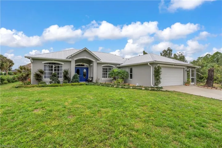 Single story home with stucco siding, concrete driveway, a front lawn, a garage, and a metal roof