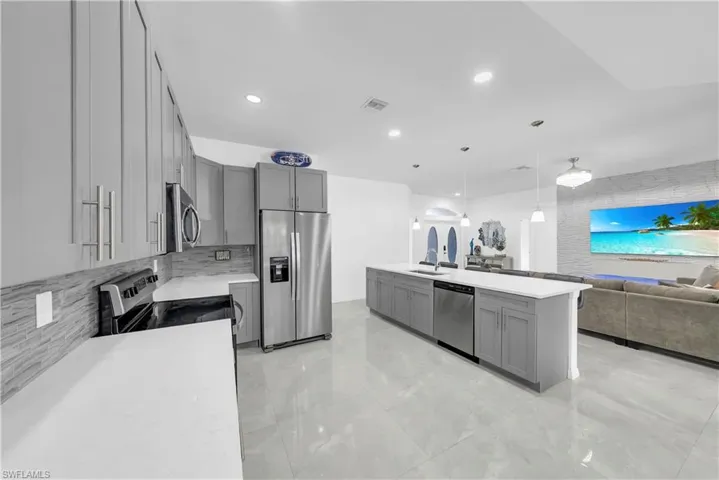 Kitchen featuring gray cabinetry, appliances with stainless steel finishes, decorative light fixtures, open floor plan, and recessed lighting
