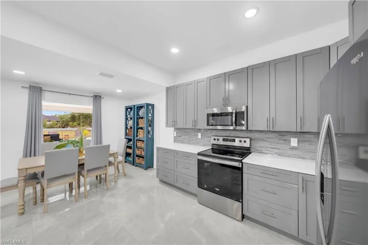 Kitchen featuring appliances with stainless steel finishes, gray cabinetry, decorative backsplash, light stone countertops, and recessed lighting