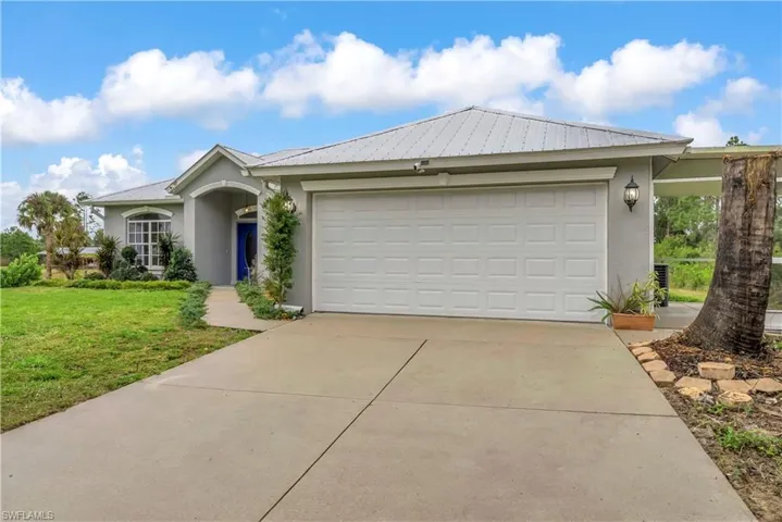 Ranch-style home with stucco siding, driveway, an attached garage, a front lawn, and a metal roof