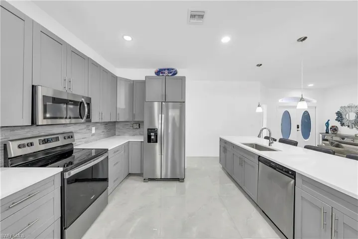 Kitchen featuring gray cabinetry, stainless steel appliances, decorative light fixtures, tasteful backsplash, and light stone counters