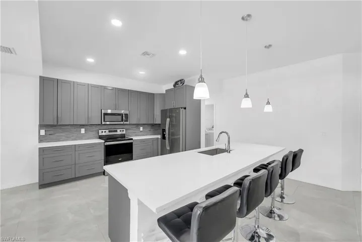 Kitchen featuring a breakfast bar area, gray cabinetry, appliances with stainless steel finishes, decorative light fixtures, and decorative backsplash