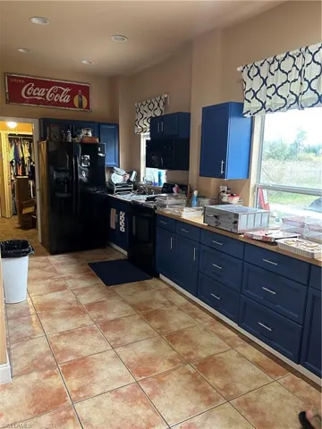 Kitchen with blue cabinets, refrigerator, black range, light tile patterned floors, and light countertops