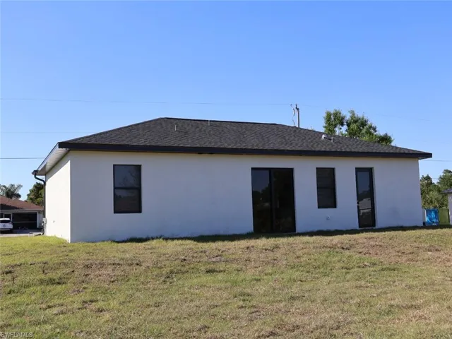 Back of house with a yard, a shingled roof, and stucco siding