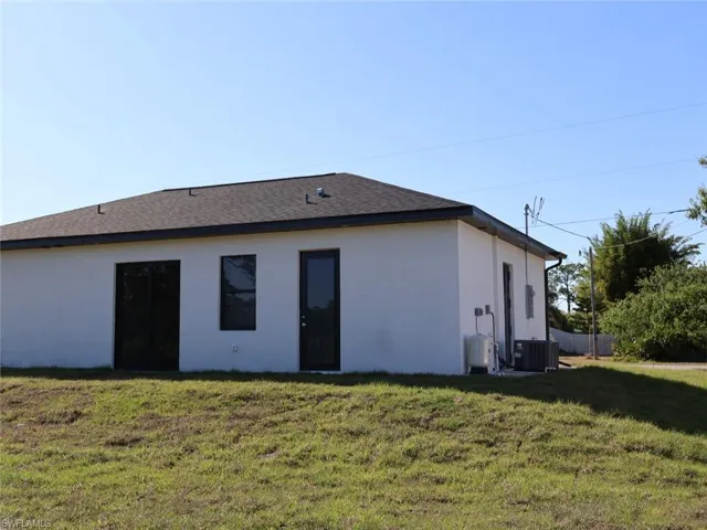 Rear view of house with central air condition unit, a lawn, and stucco siding