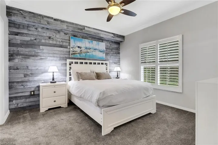 Carpeted bedroom featuring ornamental molding, ceiling fan, baseboards, and wooden walls