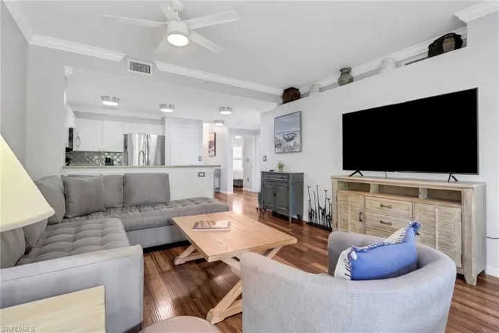 Living room with dark wood finished floors, ornamental molding, and a ceiling fan
