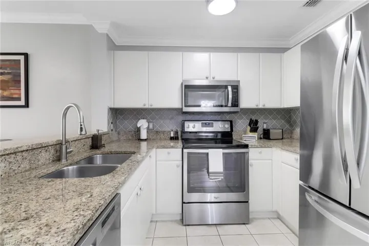 Kitchen featuring appliances with stainless steel finishes, a sink, light tile patterned flooring, ornamental molding, and tasteful backsplash