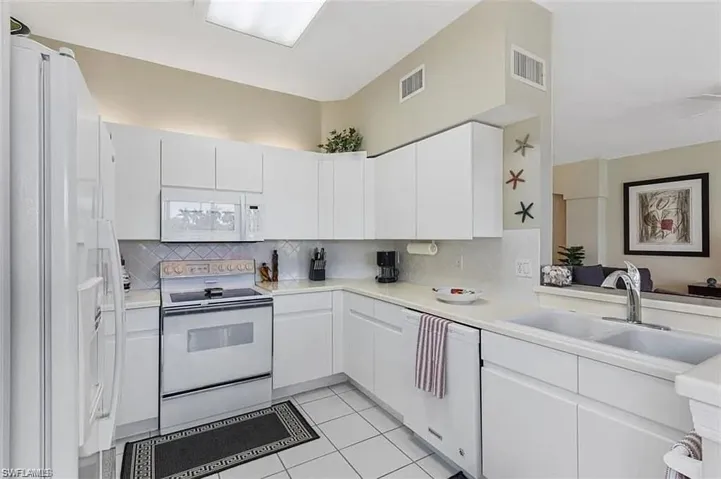 Kitchen featuring white appliances, light tile patterned floors, backsplash, sink, and white cabinetry