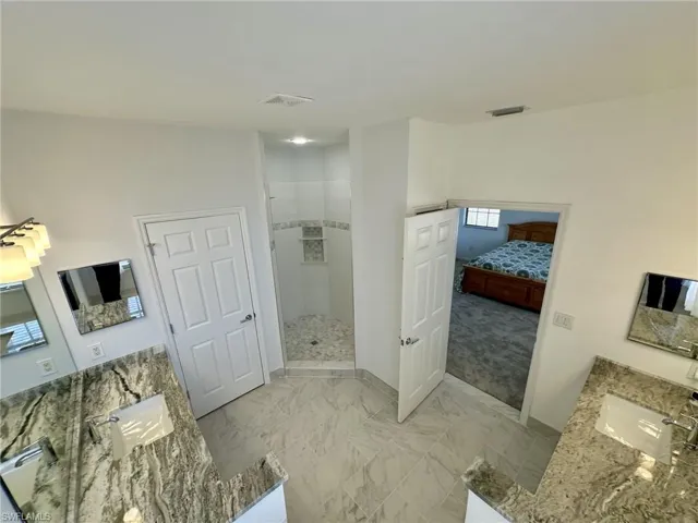 Full bath with marble finish floor, visible vents, vanity, and walk in shower