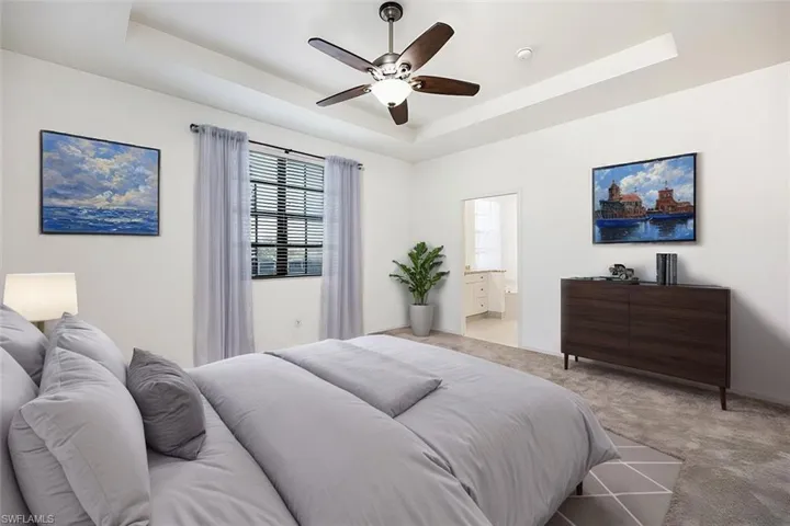 AI Staged - Bedroom featuring ceiling fan, a tray ceiling, connected bathroom, and light colored carpet