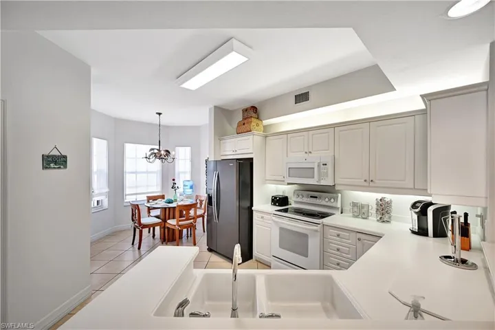 Kitchen featuring white appliances, light countertops, a chandelier, light tile patterned flooring, and white cabinetry