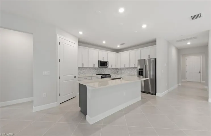 Kitchen featuring high quality appliances, an island with sink, sink, white cabinets, and backsplash
