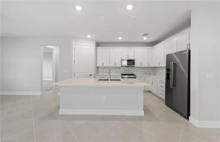 Kitchen with appliances with stainless steel finishes, sink, white cabinets, decorative backsplash, and a center island with sink