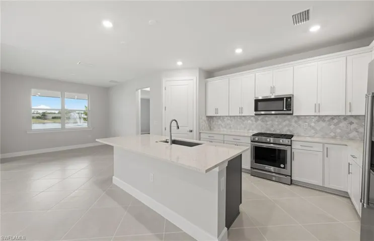 Kitchen featuring sink, white cabinetry, appliances with stainless steel finishes, an island with sink, and light stone countertops