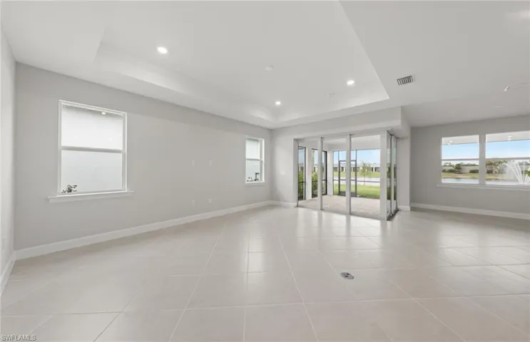 Empty room featuring light tile patterned floors, plenty of natural light, and a raised ceiling