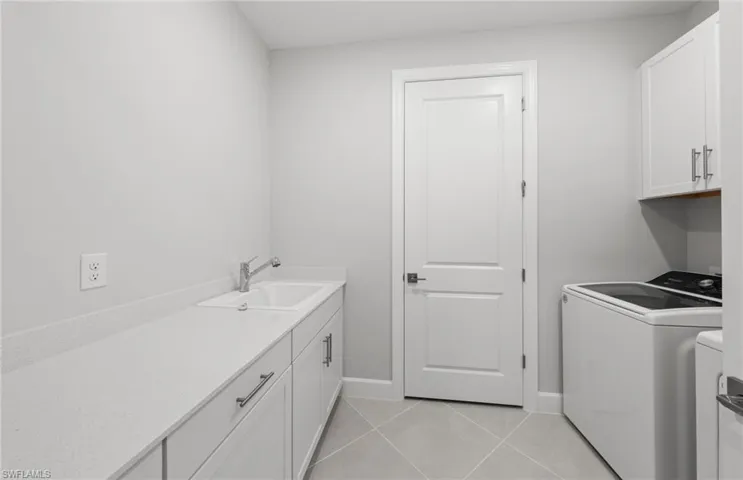 Laundry area featuring light tile patterned flooring, cabinets, sink, and washer and dryer