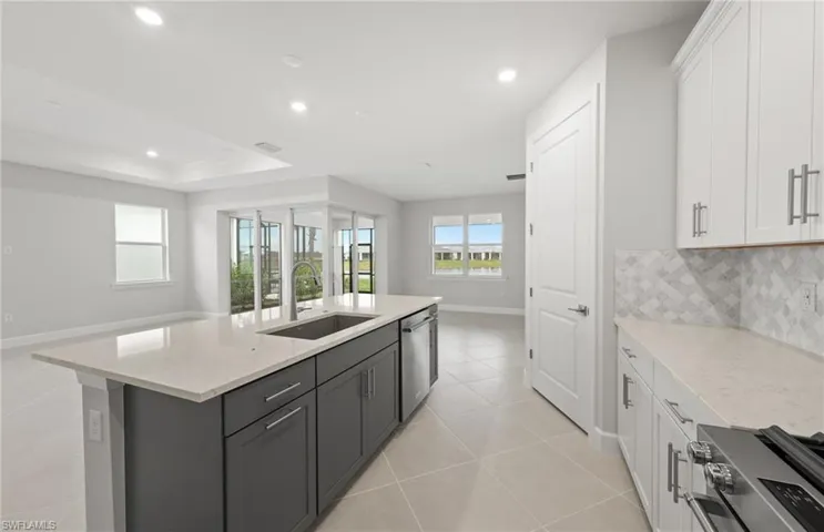 Kitchen with sink, white cabinetry, stainless steel appliances, light stone countertops, and a center island with sink