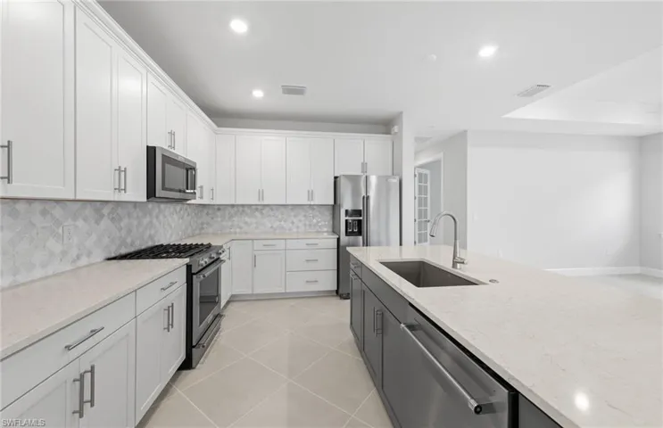 Kitchen with light tile patterned flooring, sink, white cabinetry, high quality appliances, and light stone countertops