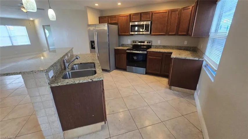Kitchen featuring appliances with stainless steel finishes, a kitchen island with sink, light tile patterned flooring, decorative light fixtures, and recessed lighting