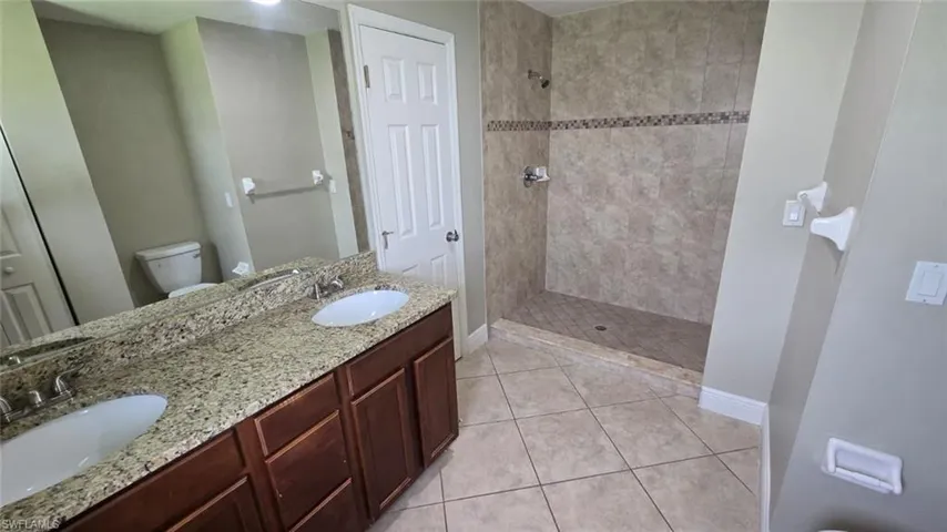 Bathroom featuring tile patterned flooring, a tile shower, and double vanity