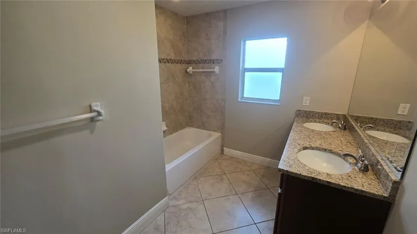 Bathroom with tile patterned floors, double vanity, and washtub / shower combination