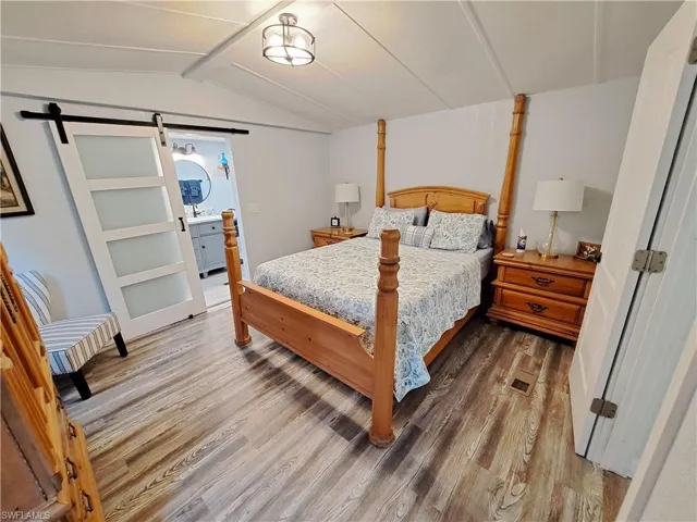 Bedroom with wood-type flooring, lofted ceiling, a barn door, and ensuite bath