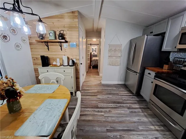 Kitchen featuring stainless steel range oven, dark hardwood / wood-style floors, wood walls, lofted ceiling with beams, and pendant lighting