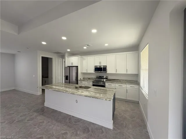 Kitchen featuring a kitchen island with sink, a sink, white cabinetry, and appliances with stainless steel finishes