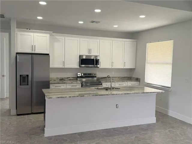 Kitchen with a sink, stainless steel appliances, a kitchen island with sink, visible vents, and white cabinets