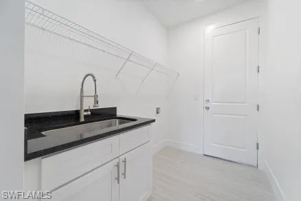 Laundry area with baseboards, cabinet space, a sink, and light wood-style floors