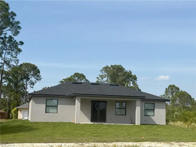 Rear view of property with roof with shingles, stucco siding, and a yard