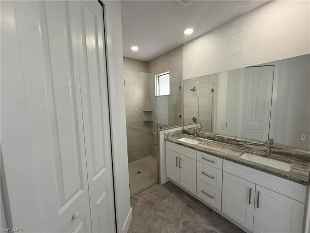Full bath featuring a shower stall, double vanity, recessed lighting, and a sink