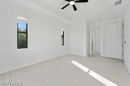 Unfurnished room with a tray ceiling, visible vents, a ceiling fan, and light wood-type flooring