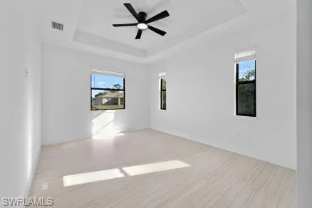 Empty room featuring a wealth of natural light, wood finished floors, ceiling fan, and a raised ceiling