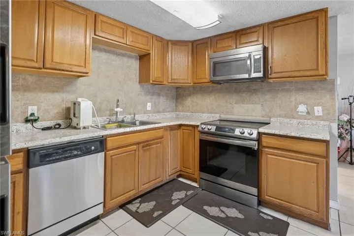 Kitchen with stainless steel appliances, wood finish cabinetry, light tile patterned floors, a textured ceiling, and decorative backsplash